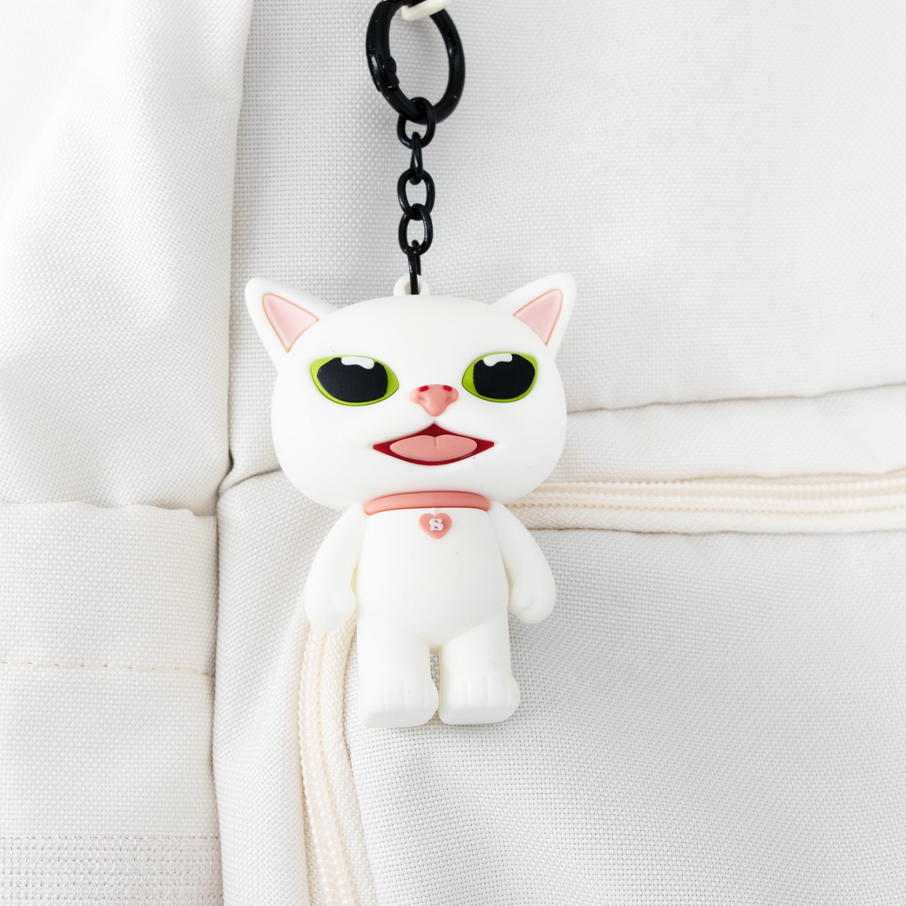 White cat-shaped keychain charm with black chain on a backpack